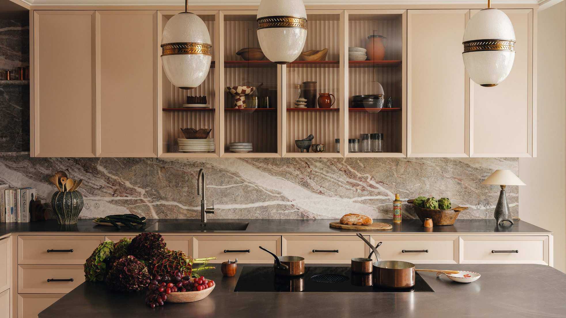 a pink modern kitchen with flat front cabinets with reeded glass upper units and a marble backsplash with a stainless stell island