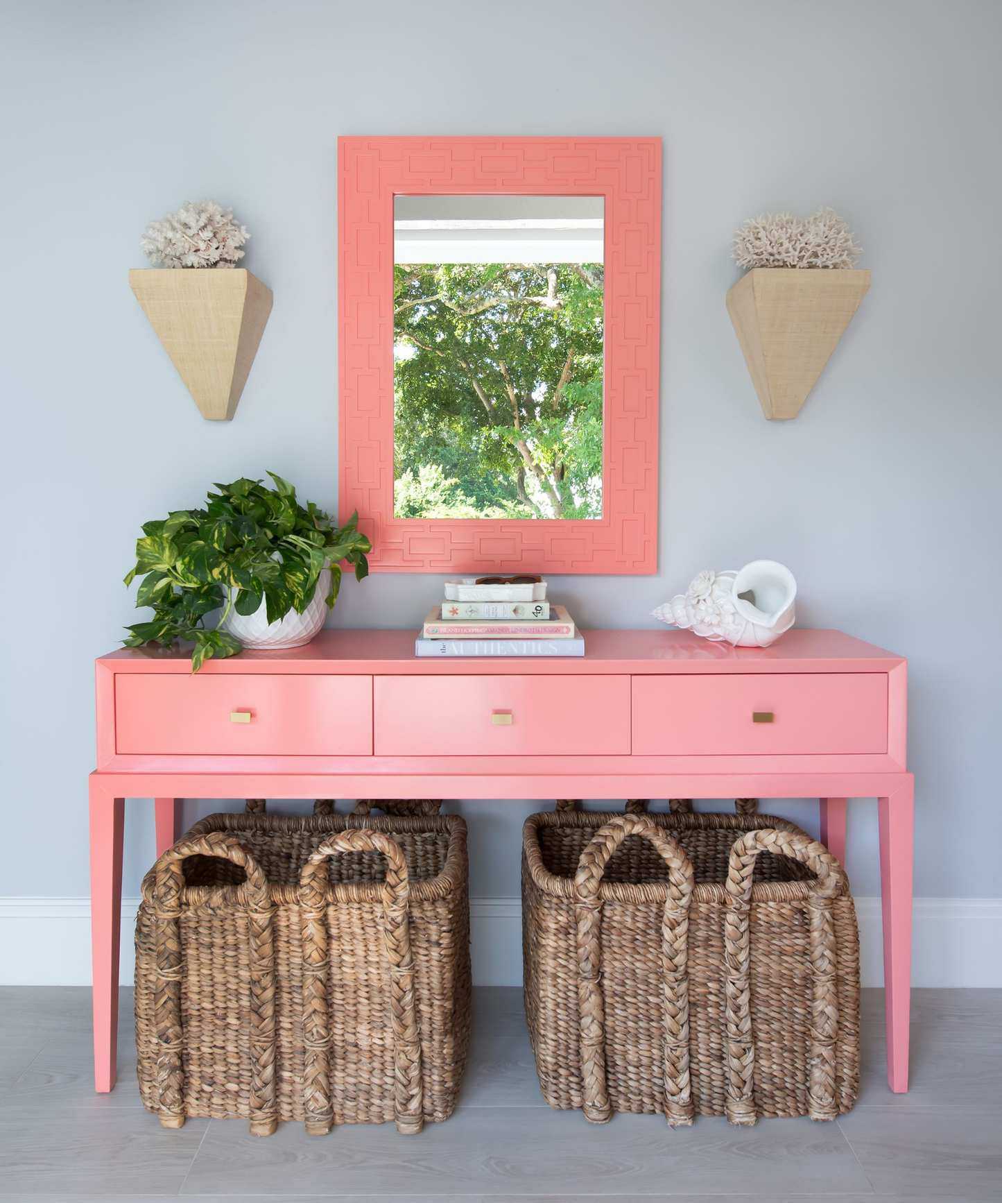 Entryway with painted pink console and matching mirror, rattan baskets, stack of books and potted plants