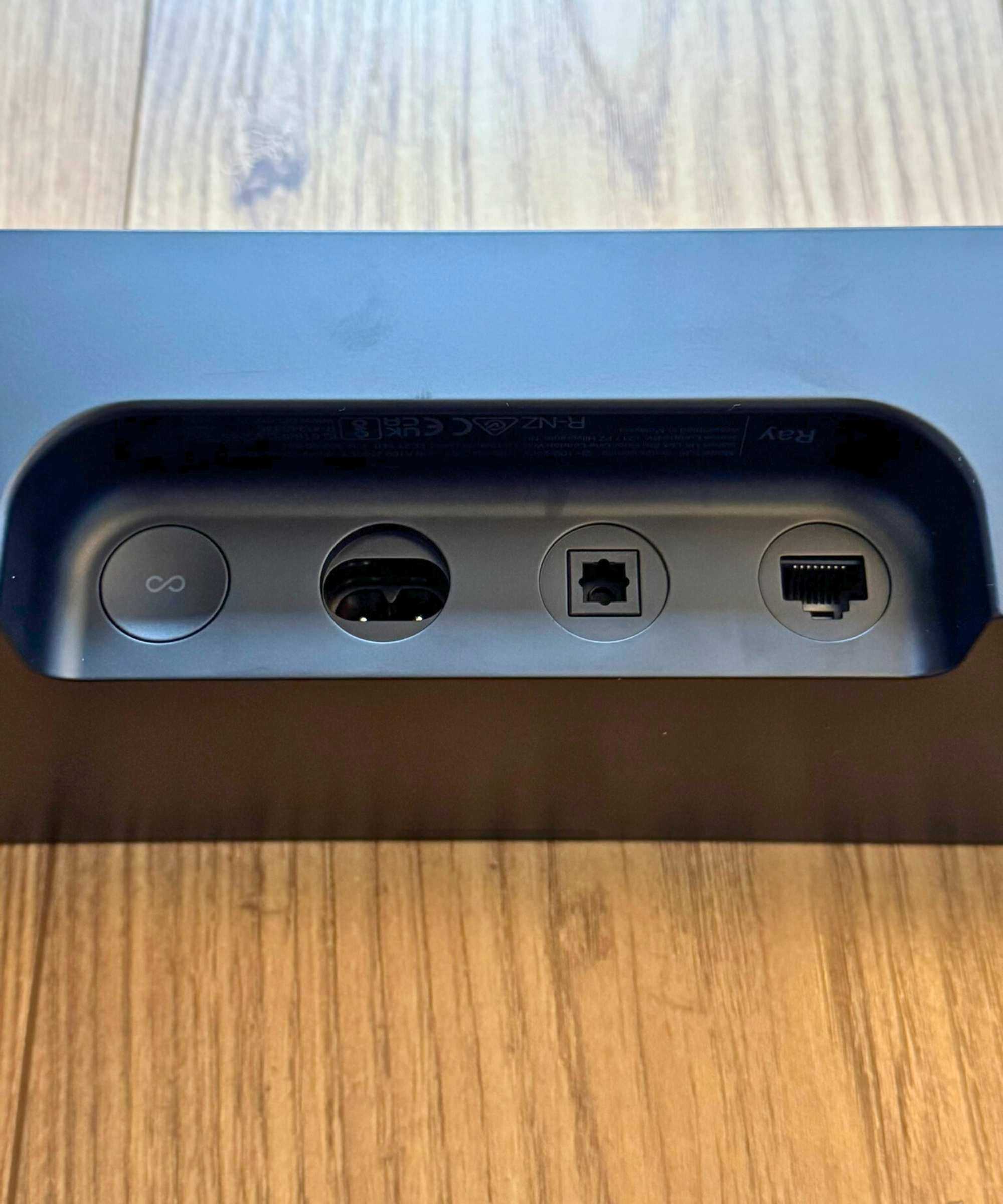 Closeup of the Sonos Ray soundbar's cable ports and button, on wooden floor.