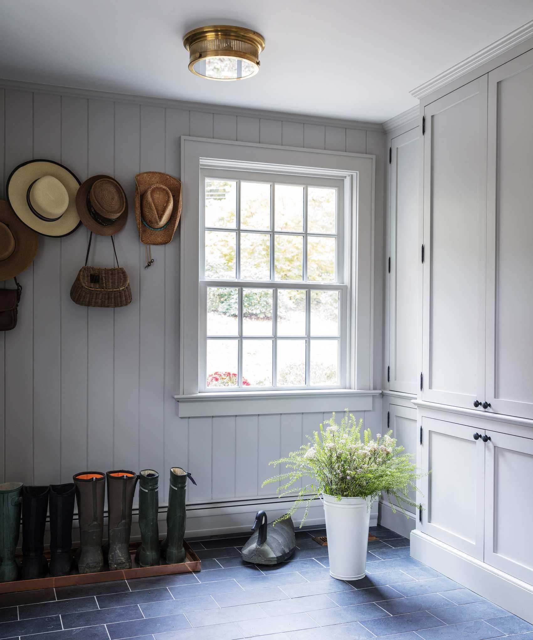 A simple mudroom with wellies storied on the floor, hats stored on coat pegs and a large window
